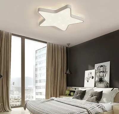 A bedroom with a star-shaped ceiling light, large windows with curtains, and a bed with pillows.