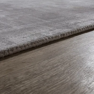 A close-up view of a gray rug with a textured surface, lying on a wooden floor.
