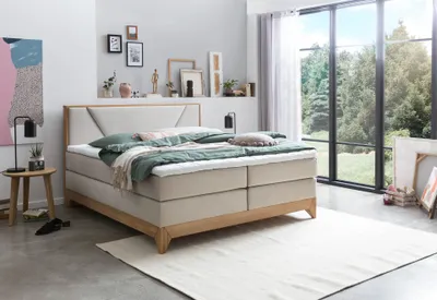 A bedroom scene with a large bed, nightstand, and a window overlooking a forest.