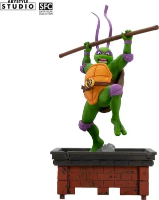A figurine of Donatello from Teenage Mutant Ninja Turtles, posed dynamically on a brick-like platform.