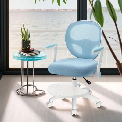 A blue ergonomic desk chair with a footrest and adjustable armrests is placed next to a small round side table with a plant and books on it, in front of a large window overlooking a body of water.