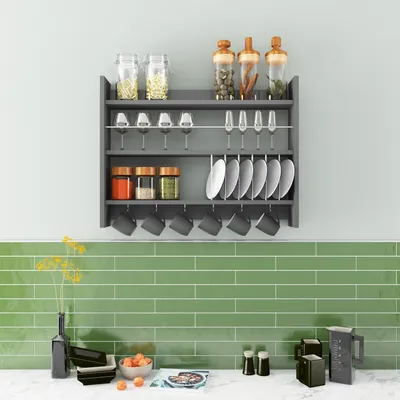 A kitchen shelf with various items like jars, glasses, plates, and mugs, set against a light gray wall and a green tiled backsplash.
