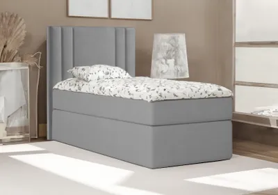A single bed with a grey upholstered base and headboard, dressed with a white and grey patterned duvet and pillow, set in a neutral-toned room.