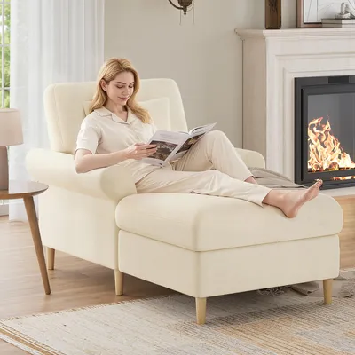 A woman is relaxing on a beige chaise lounge, reading a magazine, with a fireplace in the background.