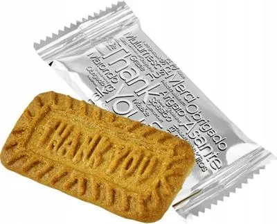 A single individually wrapped cookie with the words "Thank You" embossed on it, next to its silver wrapper which also has "Thank You" and other thank you phrases in multiple languages printed on it.
