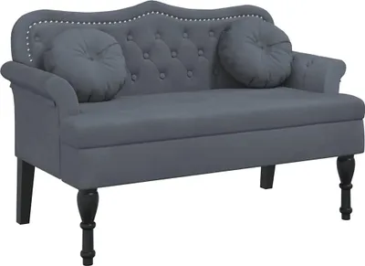 A dark gray velvet bench with tufted back and two round throw pillows, shown from the front on a white background.