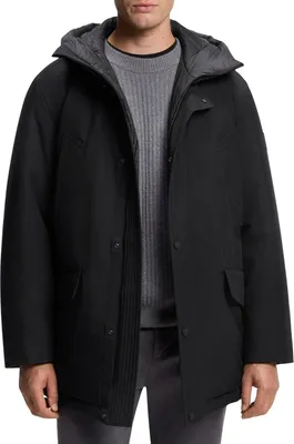 A man wearing a black hooded jacket over a grey sweater.