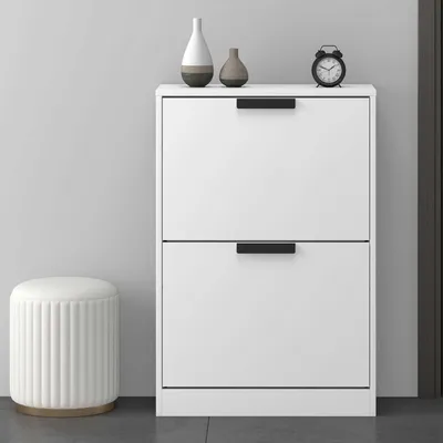 A white shoe cabinet with two drawers, a round white stool, and two decorative vases on top, placed against a light gray wall.