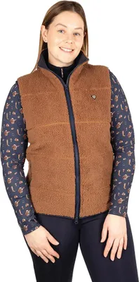 A woman is shown wearing a brown teddy fleece vest over a navy blue patterned long-sleeved shirt and navy blue pants.