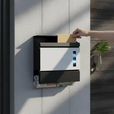 A hand is placing a letter into a modern black and white mailbox mounted on a concrete wall. The mailbox has a newspaper compartment at the bottom and three blue illuminated squares on its front.