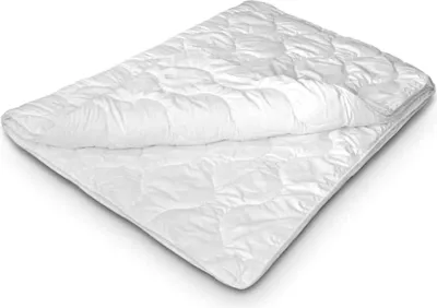 A white, quilted comforter is folded and laid out on a white surface.