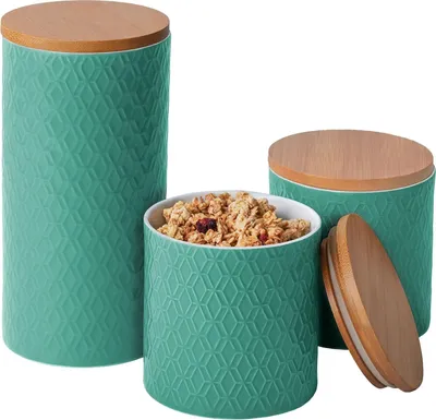 Three turquoise ceramic canisters with wooden lids are displayed against a white background. One canister is filled with granola.