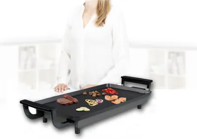 A person is standing behind an electric grill with food on it.