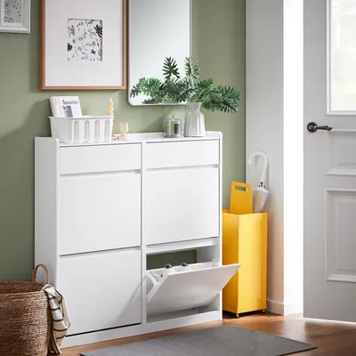 A white shoe cabinet with multiple compartments is shown in a hallway next to a door and a yellow umbrella stand.