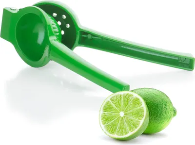 A green citrus juicer with two limes, one whole and one cut in half, are placed in front of it on a white background.