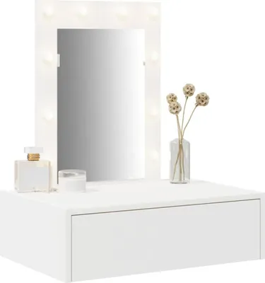 A white vanity table with a lighted mirror, a perfume bottle, a jar, and dried flowers in a vase.