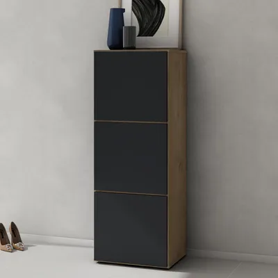 A tall, narrow shoe cabinet with a wood-grain finish on the sides and three black cabinet doors on the front, set against a light gray wall and white floor.