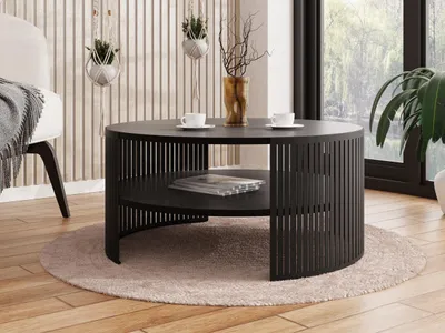 A modern living room scene featuring a black round coffee table with a slatted design and a lower shelf, placed on a light-colored rug.