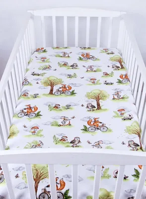 A crib sheet with a woodland animal pattern is laid out inside a white crib.
