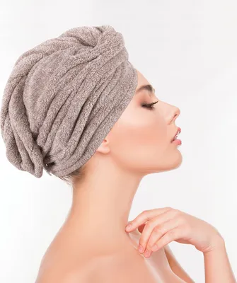 A woman wearing a brown towel turban on her head, with her hand touching her shoulder.