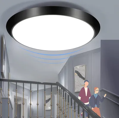 A modern hallway with a staircase, featuring a sleek ceiling light and two people walking up the stairs.