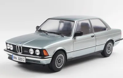 A silver and blue BMW 323I E21 1980 model car is shown from a three-quarter front angle against a white background.