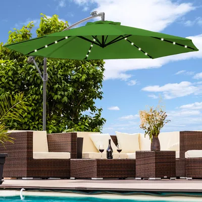 An outdoor patio scene with a green cantilever umbrella, wicker furniture, and wine glasses.