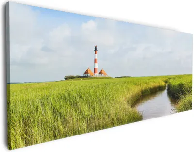 Produktbild von Wallario Premium Leinwandbild Kleiner Bach durch Schilf auf dem Weg zum Leuchtturm in Größe 60 x 150 cm