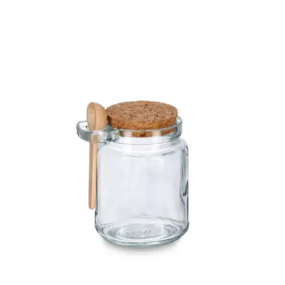 A clear glass jar with a cork lid and a small wooden spoon attached to the side.