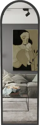 A full-length mirror with a black frame is shown in a living room setting, reflecting a couch, coffee table, and artwork.