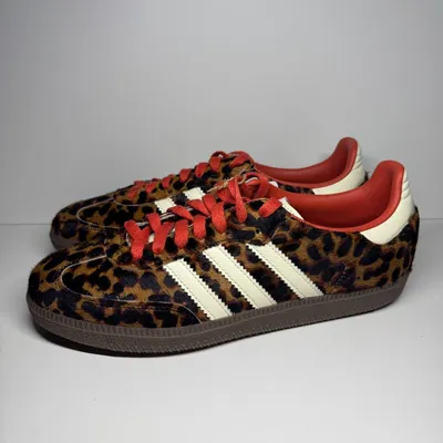 A pair of Adidas Samba OG sneakers with a leopard print pattern and red laces, displayed against a neutral background.