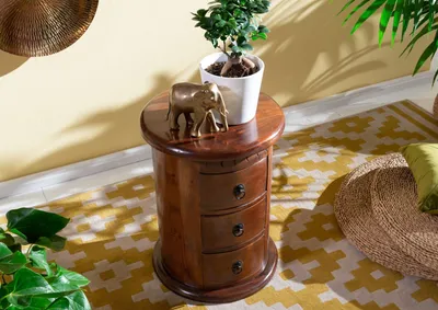 A wooden nightstand with drawers, decorated with a golden elephant figurine and a potted plant, placed on a patterned rug.