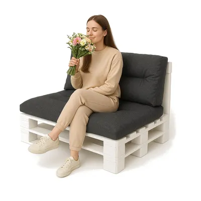 A woman sits on a pallet sofa, smelling a bouquet of flowers.