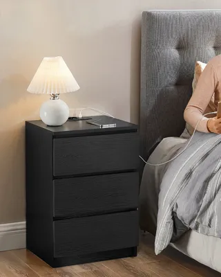 A person is in bed next to a nightstand with a lamp and a phone.