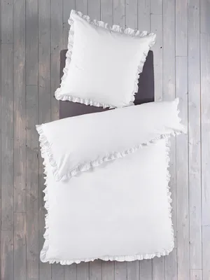 A top-down view of white bedding with ruffles, laid out on a wooden floor.
