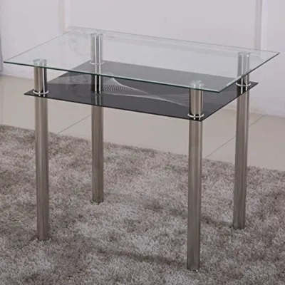 A glass-top dining table with a black lower shelf and silver legs, placed on a grey carpet.
