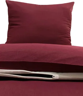A close-up view of a burgundy duvet cover and pillowcase set, showing the texture of the fabric and a zipper closure.