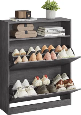 A grey shoe cabinet with multiple shelves and flip-down doors, filled with various shoes. A small plant sits on top of the cabinet.