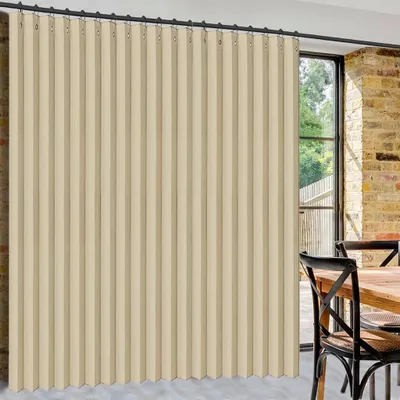A beige vertical blind is shown covering a large window in a room with exposed brick walls and a wooden table with chairs.