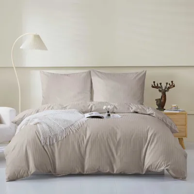 A neatly made bed with taupe bedding and two pillows, a white throw blanket, and a book on the bed. A floor lamp is on the left, and a nightstand with a deer figurine and a cup is on the right.