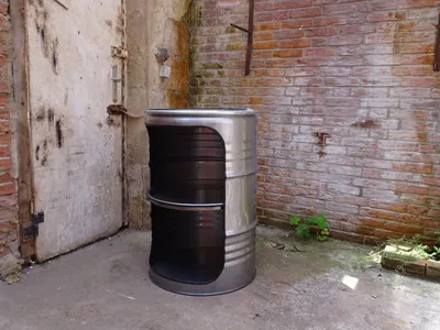A metal barrel converted into a shelf unit, placed in an outdoor area with a brick wall and a weathered door.