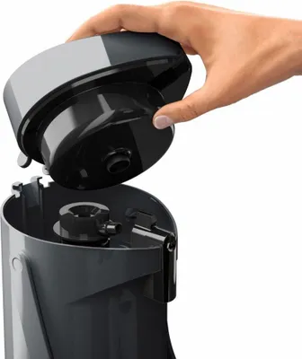 A hand is shown removing the lid from a gray and black appliance.
