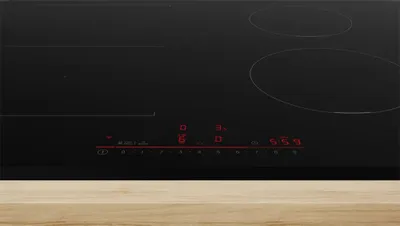 A close-up shot of a black induction cooktop with red digital displays.