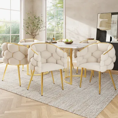 A dining room scene with a marble-topped table and six beige velvet chairs with gold legs.