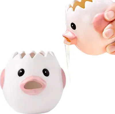 A hand is holding a ceramic egg separator shaped like a chick, with egg yolk dripping into another ceramic chick-shaped egg separator below.