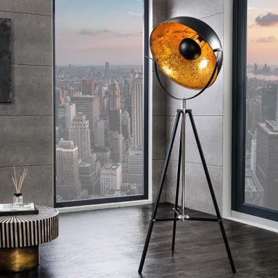 A modern floor lamp with a gold interior is placed in a room with a large window overlooking a city skyline.