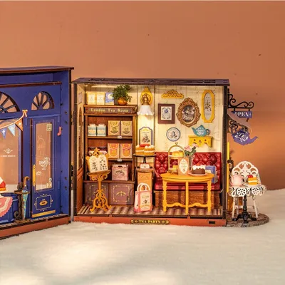 A miniature dollhouse tea room with detailed furniture and accessories, set against a plain background.