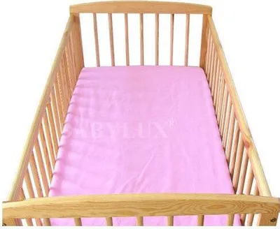 A pink crib sheet inside a wooden crib.