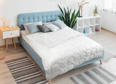 A bedroom scene with a bed, nightstand, and plant.