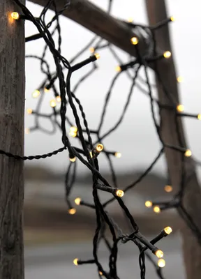 A close-up of a string of warm white LED lights wrapped around wooden poles.